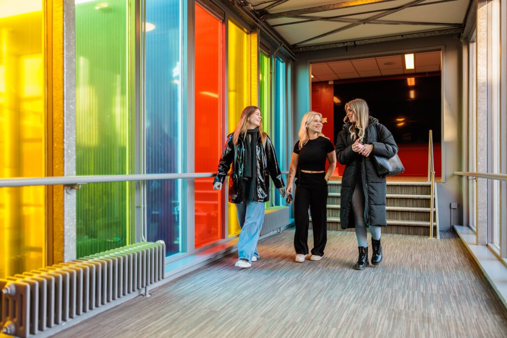 Studenten wandelend door gekleurd glazen loopbrug in het pand van Noorderpoort Kunst & Multimedia.